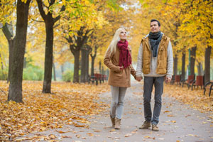 A couple holding hands and walking through a park in fall
