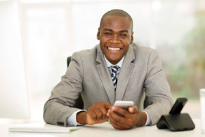 A man sitting at a desk, smiling, holding a phone in his hand.