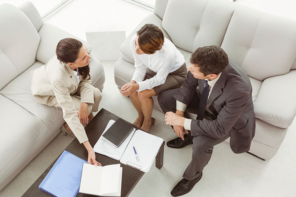 3 people sitting on couches discussing paper work